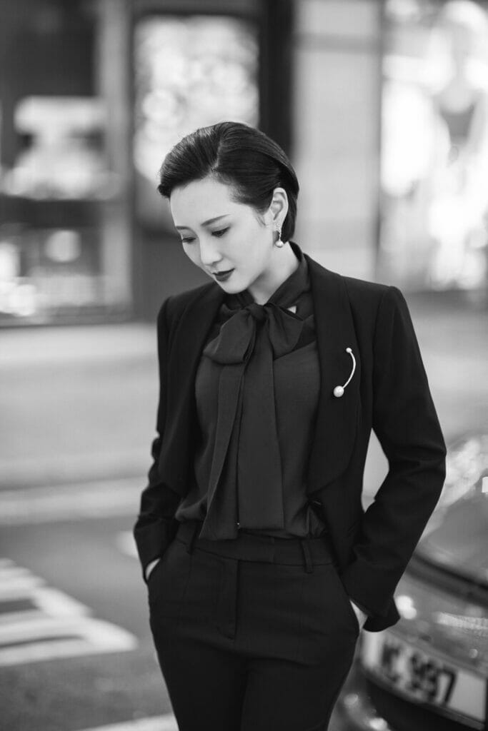 A woman in a black suit standing on a street.