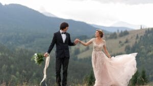 A bride and groom are holding hands in the mountains.