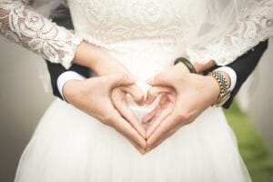 A bride and groom making a heart shape with their hands.